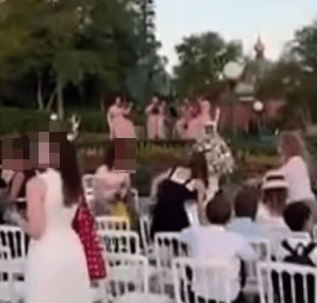 People seated at white chairs outdoors watching a performance.