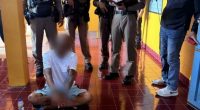 A Buddhist monk sits on the floor surrounded by police officers.