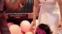 A toddler girl receives a car key from her parents in front of a pink Rolls Royce.