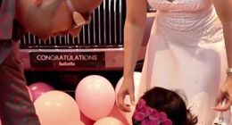 A toddler girl receives a car key from her parents in front of a pink Rolls Royce.
