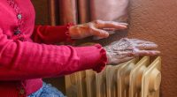 Elderly person's hands warming themselves on a radiator.