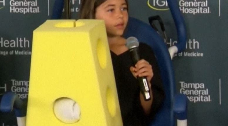 Girl holding microphone, wearing a yellow foam block costume.