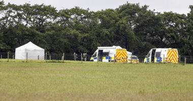 Crime scene with police vehicles and a tent in a field.