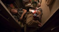 Elderly man sleeping in a small, cluttered room.