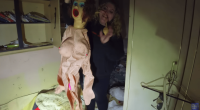 Woman holding up a sex doll in a dilapidated room.