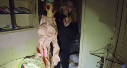 Woman holding up a sex doll in a dilapidated room.