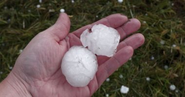 Hand holding two large hailstones after a storm.
