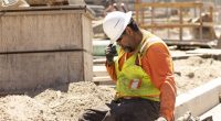 A construction worker sits and puts his head down, still in the hot sun.