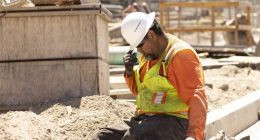 A construction worker sits and puts his head down, still in the hot sun.