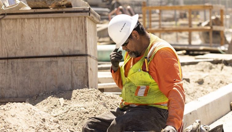 A construction worker sits and puts his head down, still in the hot sun.