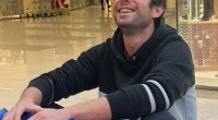 A smiling man sitting on a blue bumper car in a shopping mall.