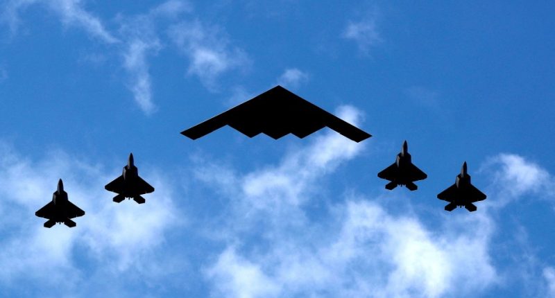 B-2 Spirit bomber flanked by four F-22 Raptor fighter jets.