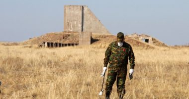 A man in camouflage clothing measures radiation levels near the remains of a structure.