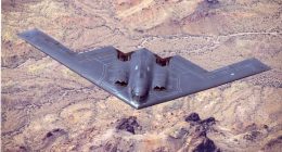 B-2 Spirit stealth bomber in flight over desert terrain.