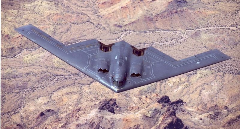 B-2 Spirit stealth bomber in flight over desert terrain.