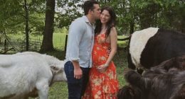 Pregnant woman in orange dress being kissed by a man, with cattle nearby.