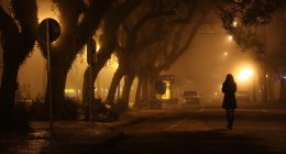 Silhouette of a woman walking down a foggy street at night.