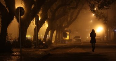 Silhouette of a woman walking down a foggy street at night.
