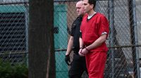 Bryan Kohberger in handcuffs, wearing a red jumpsuit, escorted by a law enforcement officer.
