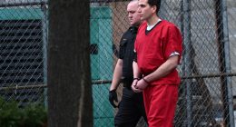 Bryan Kohberger in handcuffs, wearing a red jumpsuit, escorted by a law enforcement officer.