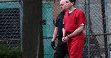 Bryan Kohberger in handcuffs, wearing a red jumpsuit, escorted by a law enforcement officer.