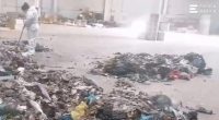 A worker in a protective suit sweeps near a pile of trash at a recycling center.