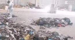 A worker in a protective suit sweeps near a pile of trash at a recycling center.