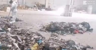 A worker in a protective suit sweeps near a pile of trash at a recycling center.