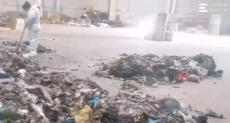 A worker in a protective suit sweeps near a pile of trash at a recycling center.