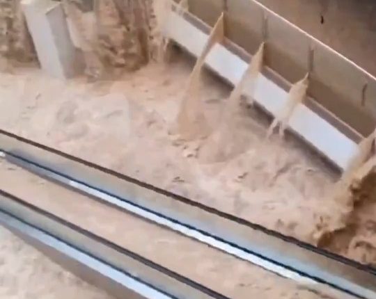 Floodwaters rushing through a shopping mall, submerging escalators.