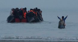 Migrants in a small boat approaching the shore.