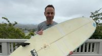 Man holding surfboard with shark bite damage.
