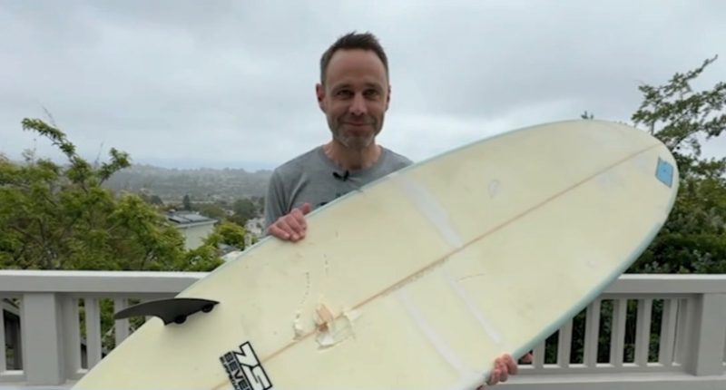 Man holding surfboard with shark bite damage.