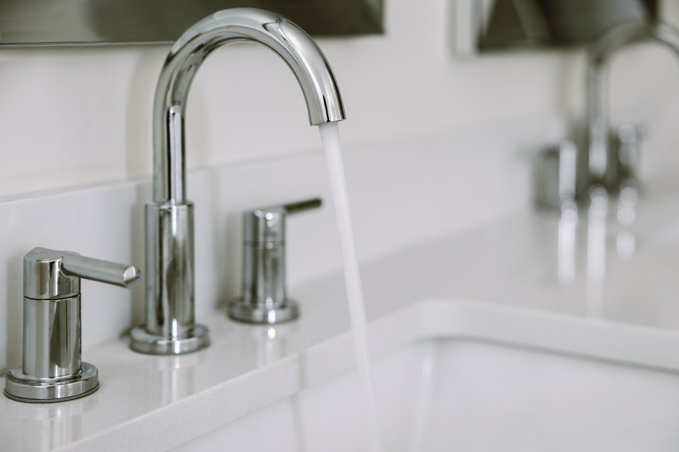 Close-up of water running from a bathroom sink faucet.