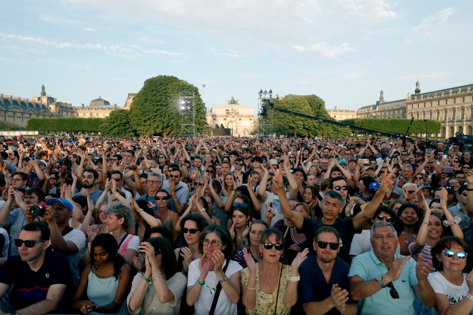 People clap as they gather to listen to music prior to the reinstallation and lift-off of the 2024 Olympic cauldron during a free concert to mark France's annual street music festival, 'Fete de la Musique', at the Jardin des Tuileries, in Paris on June 21, 2025. (Photo by GEOFFROY VAN DER HASSELT / AFP) (Photo by GEOFFROY VAN DER HASSELT/AFP via Getty Images)