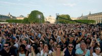 People clap as they gather to listen to music prior to the reinstallation and lift-off of the 2024 Olympic cauldron during a free concert to mark France's annual street music festival, 'Fete de la Musique', at the Jardin des Tuileries, in Paris on June 21, 2025. (Photo by GEOFFROY VAN DER HASSELT / AFP) (Photo by GEOFFROY VAN DER HASSELT/AFP via Getty Images)