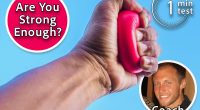 Coach Caleb Herman, The 1-Minute Grip Test That Reveals Your Real Fitness Level, cover, Red heart shaped stress ball squeezed in a hand against a clear blue sky with scattered clouds