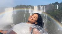 Woman in a plastic poncho smiling in front of a waterfall with a rainbow.