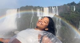 Woman in a plastic poncho smiling in front of a waterfall with a rainbow.