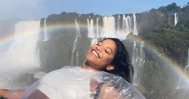 Woman in a plastic poncho smiling in front of a waterfall with a rainbow.