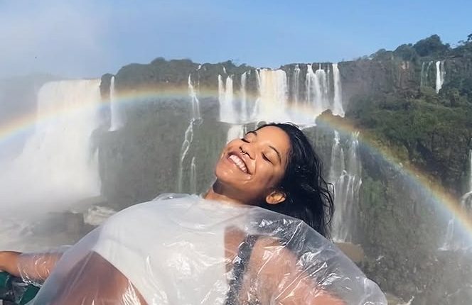 Woman in a plastic poncho smiling in front of a waterfall with a rainbow.