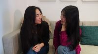 Two young women sitting on a couch, talking.