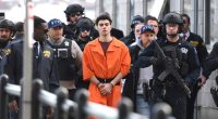 A young man wearing a bulletproof vest sits in a courtroom.
