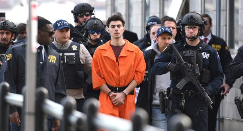 A young man wearing a bulletproof vest sits in a courtroom.