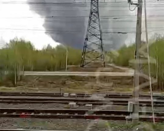 Large plume of smoke rising near a railway and power lines.