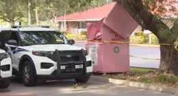 Police cars at a crime scene near a pink clothing and shoe donation bin.