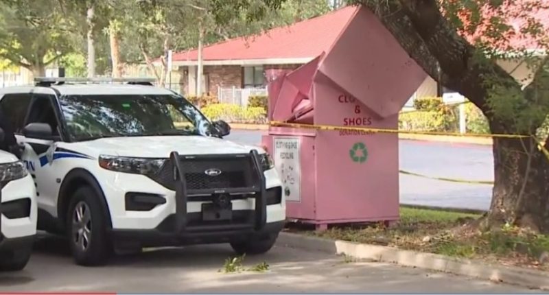 Police cars at a crime scene near a pink clothing and shoe donation bin.