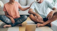 Beautiful mature couple sitting on the floor and practicing yoga. Sporty couple using digital tablet for online yoga lessons.
