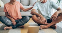 Beautiful mature couple sitting on the floor and practicing yoga. Sporty couple using digital tablet for online yoga lessons.