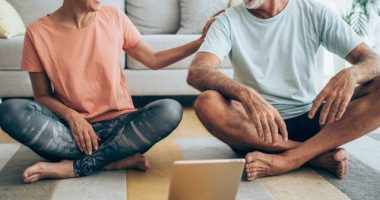 Beautiful mature couple sitting on the floor and practicing yoga. Sporty couple using digital tablet for online yoga lessons.